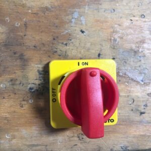 Yellow rotary switch with red handle on wooden surface.