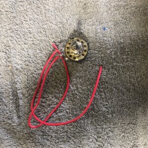 Round pendant with intricate design on red cord necklace.