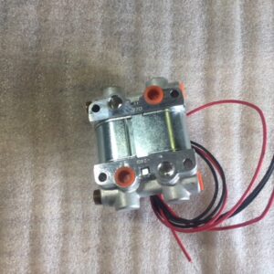 Small metallic solenoid valve with attached wires on a textured surface.