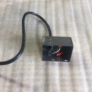 Small black electrical box with wires and a cable on a fabric surface.