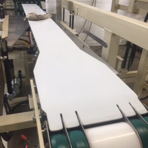 A white flat sheet on a conveyor belt in a factory.