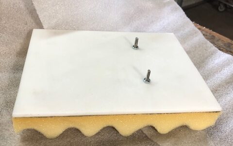 White foam panel with yellow base and two screws on top.