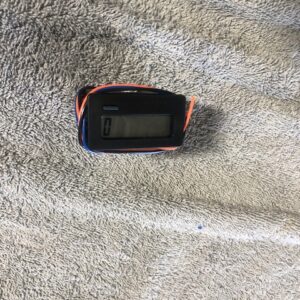 A small digital device with wires on a textured surface.