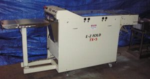 Industrial L-K fold TX-3 paper folding machine in a workshop.